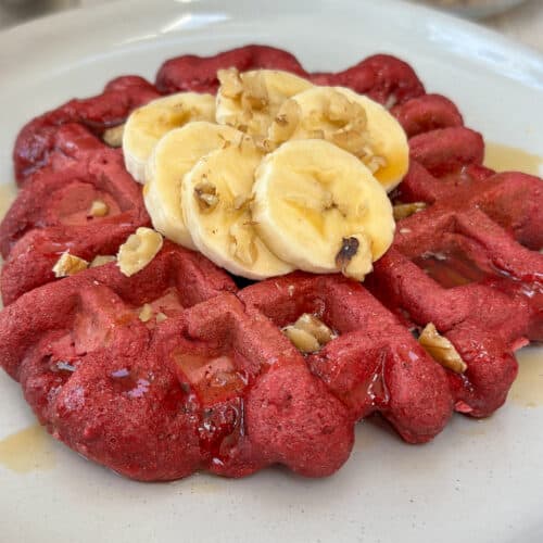 Beet waffle topped with sliced bananas, maple syrup and chopped walnuts.