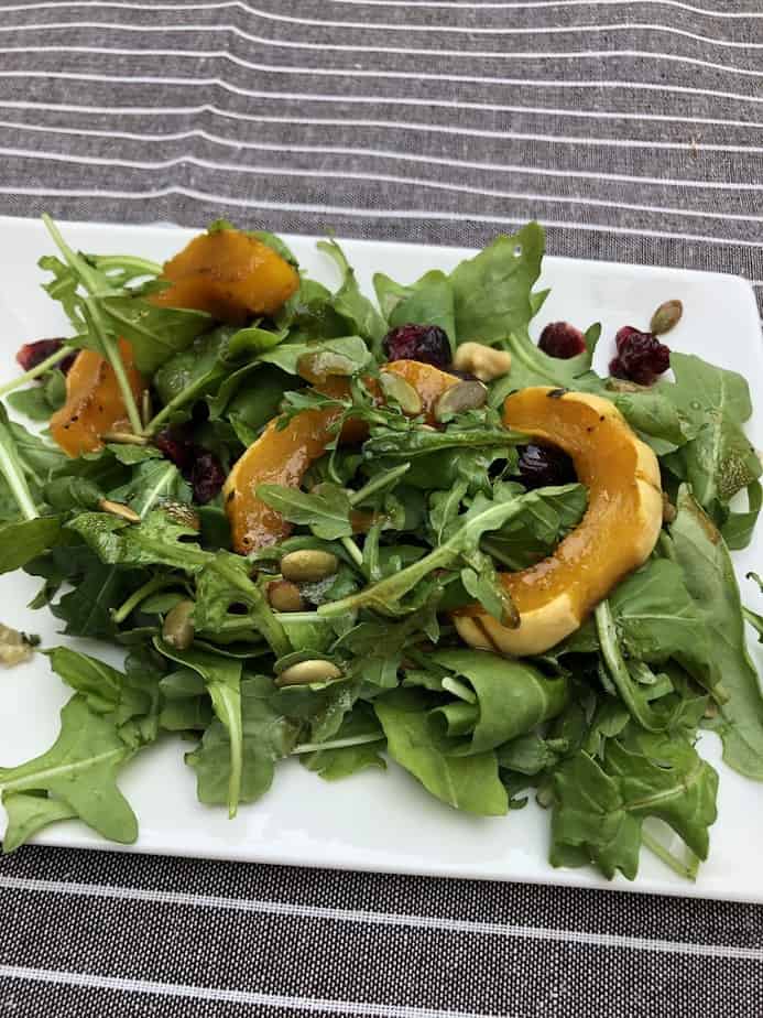 Arugula salad with roasted delicata squash, dried cranberries, and pumpkin seeds on a white plate 