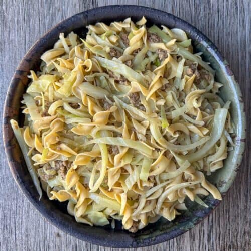 Cabbage and noodles with vegan sausage in a dark ceramic serving bowl.