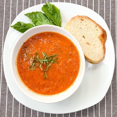 Roasted tomato soup in a white bowl with bread on a white plate.