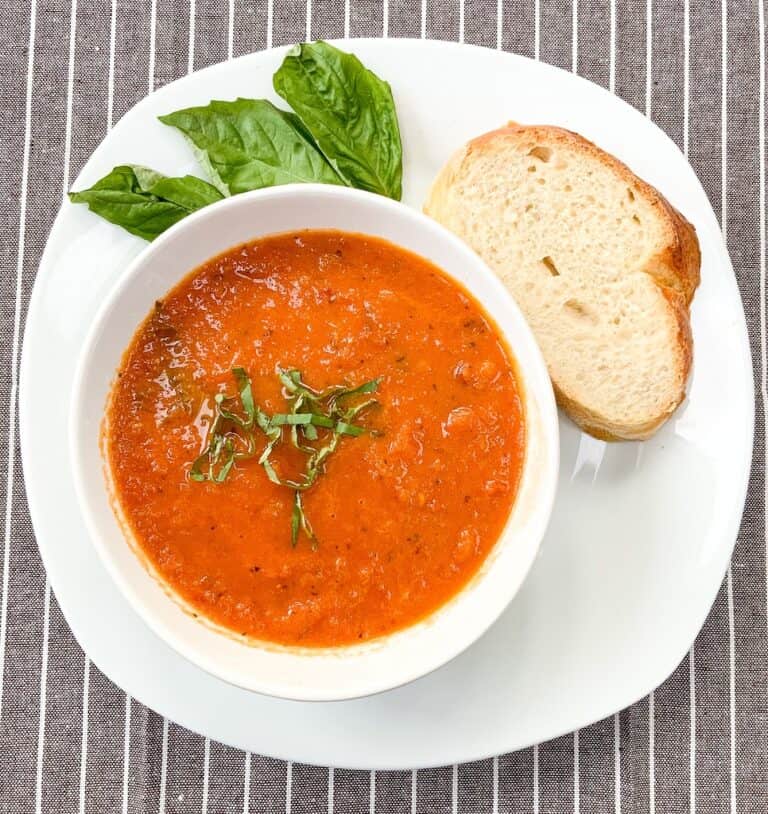 Roasted tomato soup in a white bowl with bread on a white plate.