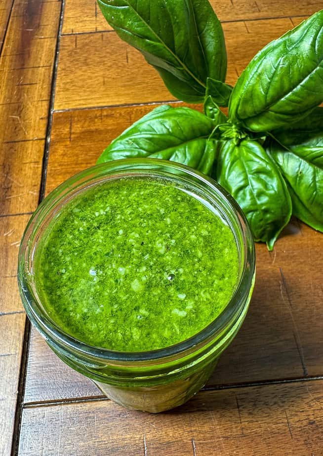 Clear glass container filled with homemade basil pesto with fresh basil leaves on the surface.