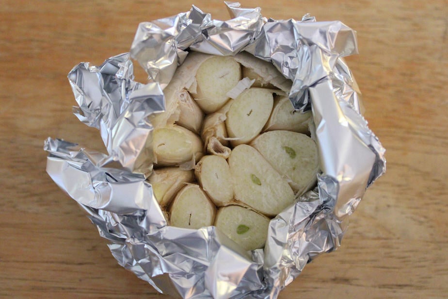 Uncooked whole garlic bulb with top sliced off and wrapped in aluminum foil. 