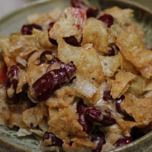 Red kidney beans with a sauce, cheese and crushed tortilla chips on top in a ceramic bowl.