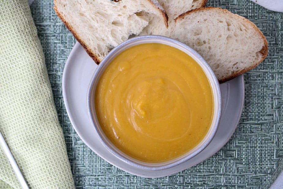 Creamy butternut squash soup in a bowl with pieces of bread to the side of the bowl.