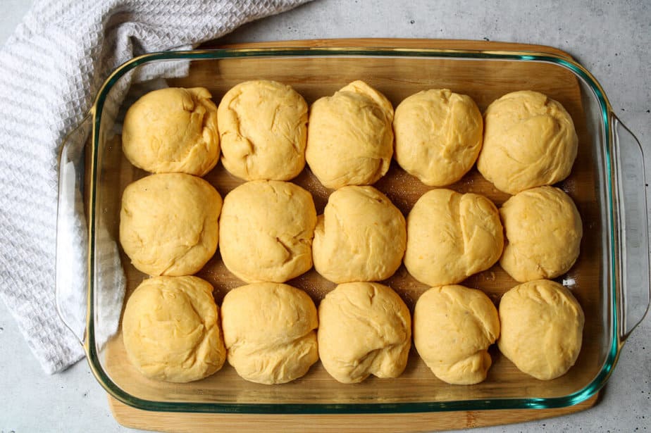 Pumpkin dinner roll dough rising in a glass baking dish.