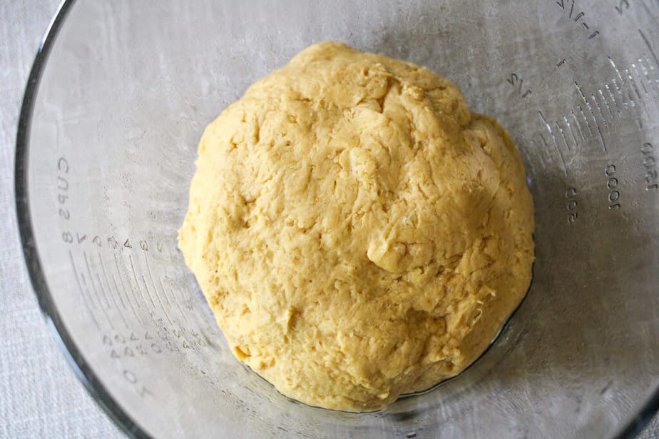 Pumpkin dinner roll dough shaped in a large ball in a clear glass bowl.