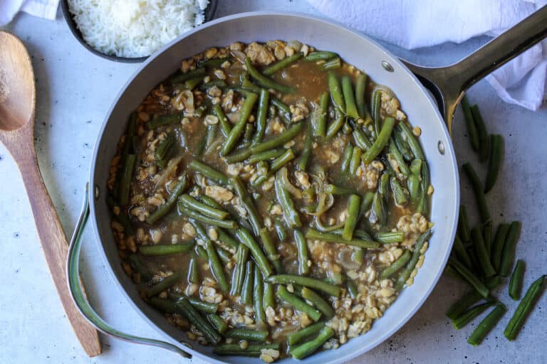 Tempeh and green beans in a large pan with a small bowl of white rice at the top left.