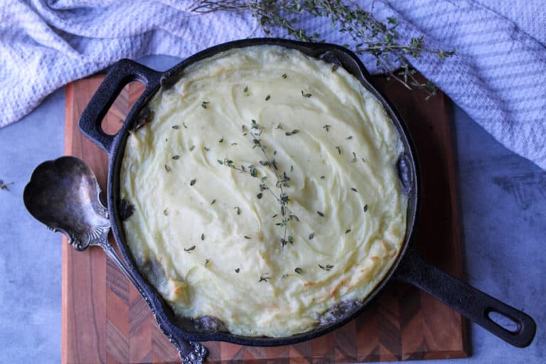 Lentil and Mushroom Shepherd's pie in cast iron skillet. Mashed potatoes on top are golden brown with sprinkles of fresh thyme on top.