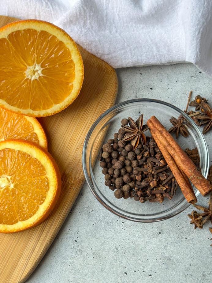 Mulling spices in a small clear glass bowl with fresh orange slices to the left.