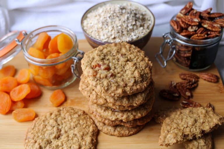 Oatmeal apricot cookies stacked with quick oats, apricots, and pecans in background.