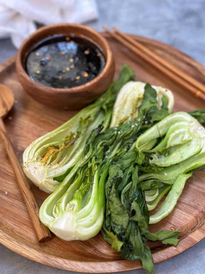 Air fried Baby Bok Choy on a wooden plate with small wooden bowl filled with dipping sauce.