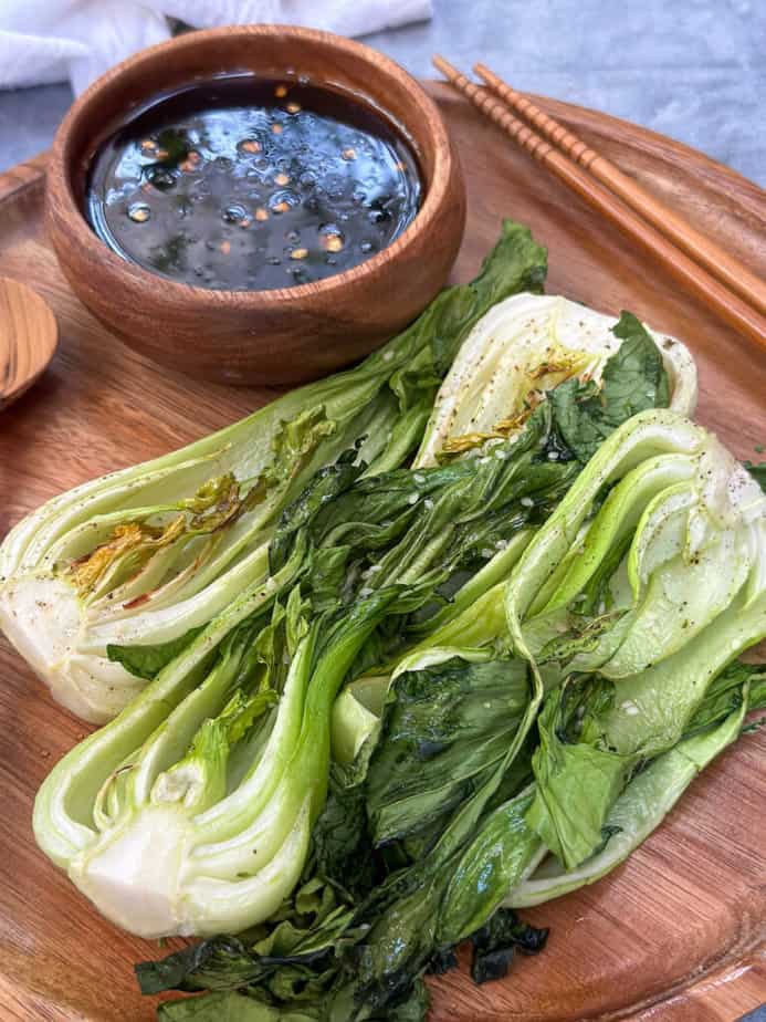 Air fried Baby Bok Choy on a wooden plate with small wooden bowl filled with dipping sauce.