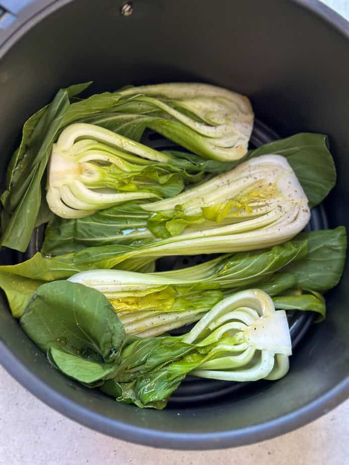 Baby bok choy halved and placed in a single layer in an air fryer basket.