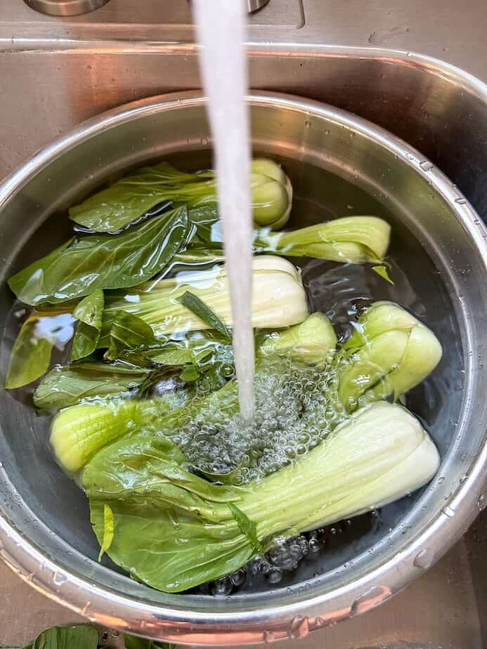 Several bok choys sliced in half in a metal bowl being filled with water. 