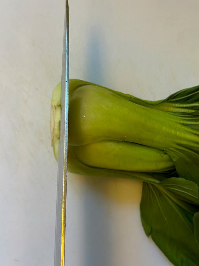 Knife slicing the end of the stem of a green baby Bok Choy.