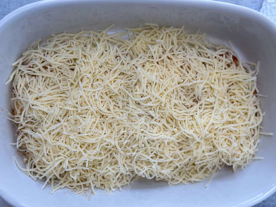 Shredded Swiss cheese over plant-based chicken patties in a white baking dish.
