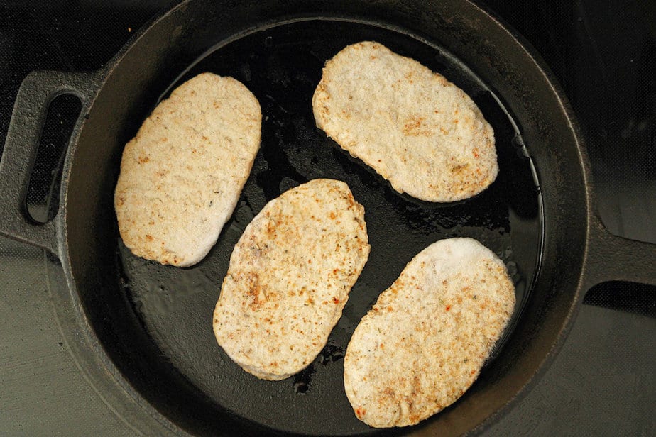 Four plant-based chicken patties sautéing in a cast iron skillet.