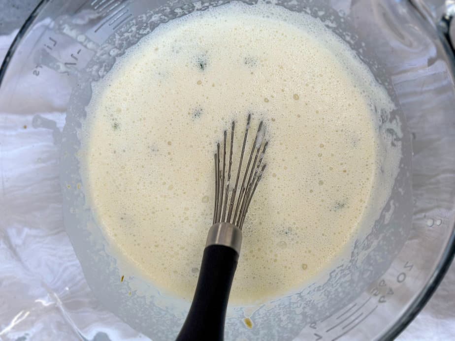 Cream sauce in a clear glass mixing bowl with a metal whisk.