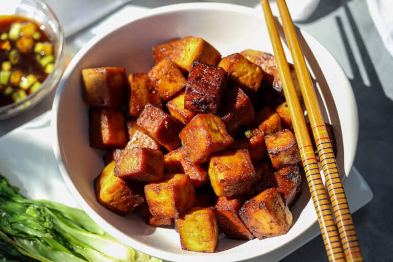 Cubed tofu that is crispy brown in white bowl with chopsticks to the side of bowl.