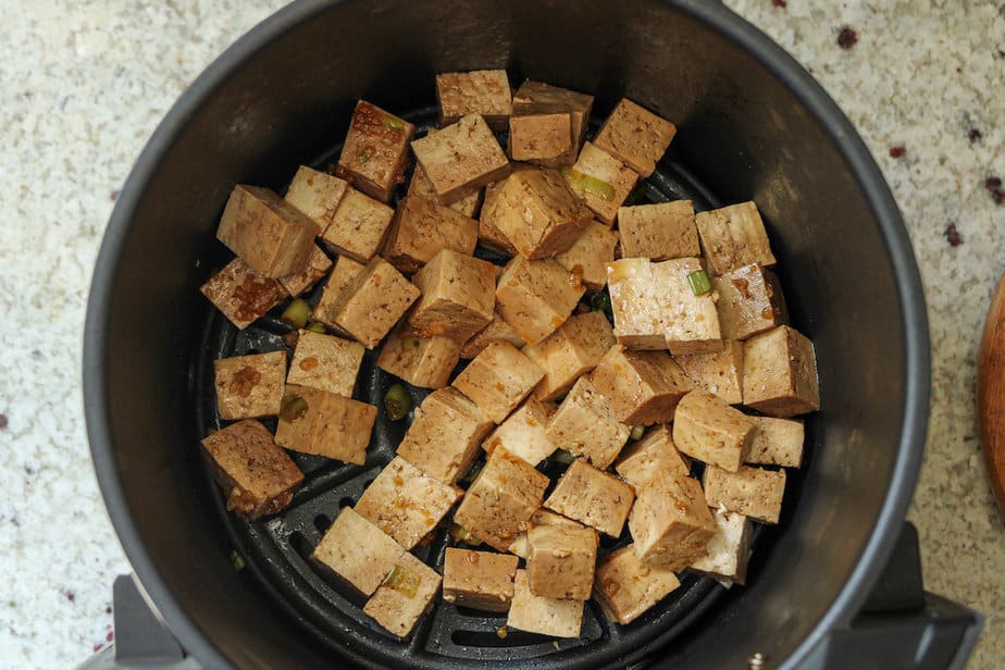 Cubed marinated tofu in an air fryer basket.