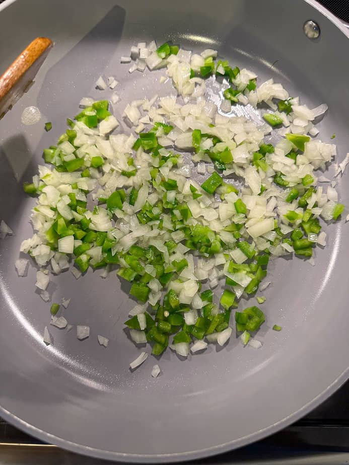Chopped onions and green pepper sautéing in a skillet.