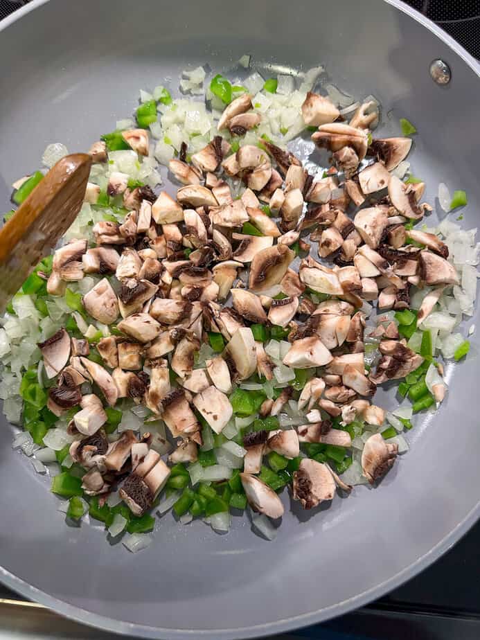 Chopped onions, green pepper and mushrooms sautéing in a skillet. 