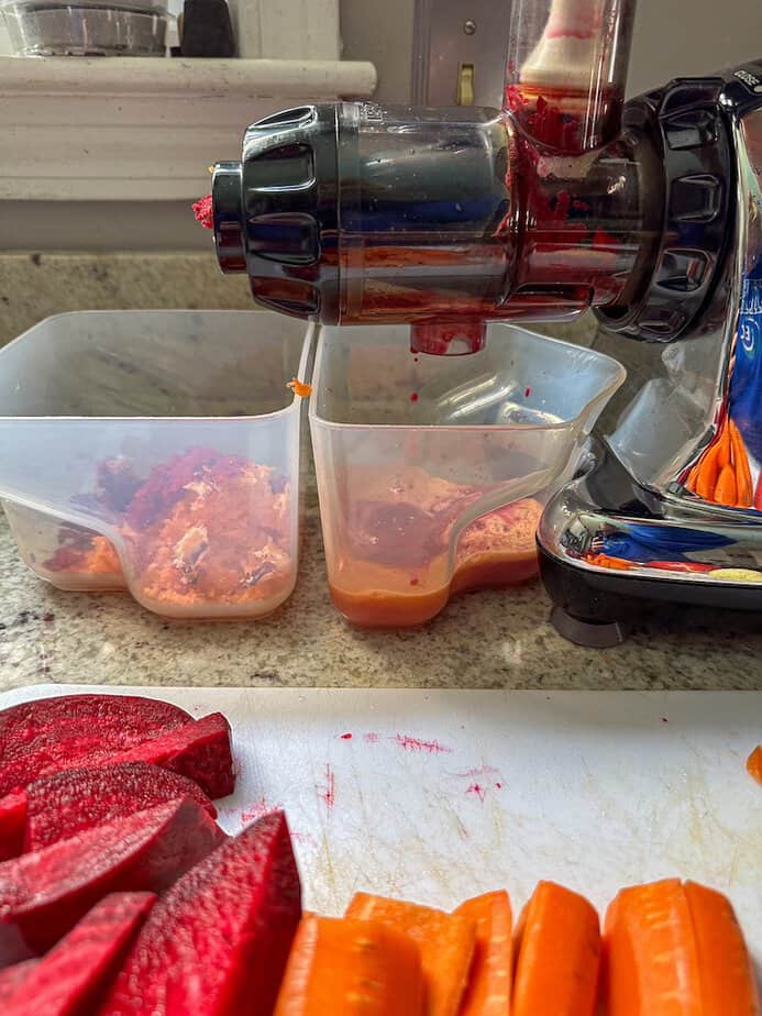 Side view of juicer with sliced beets, carrots and apple that have been run through the machine. Juice in one container and pulpit the other.