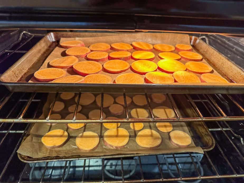 Two baking sheets in oven with sliced sweet potatoes on baking sheets line with parchment paper.