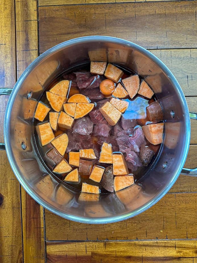 Stew beef, Chopped sweet potatoes, chopped carrots and rice covered with water in large pot.