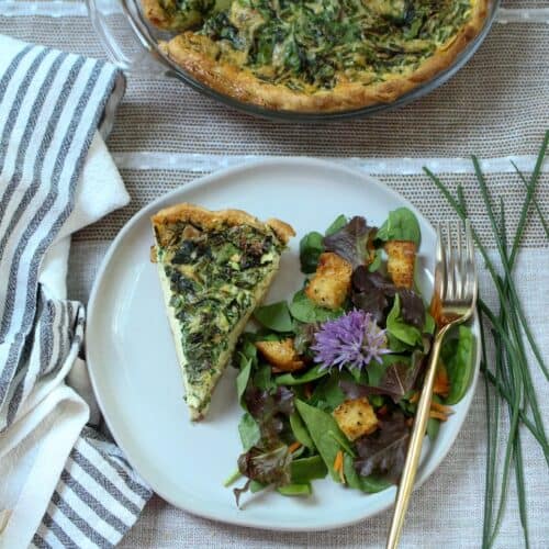 Slice of quiche on a plate with a salad to the side on plate.