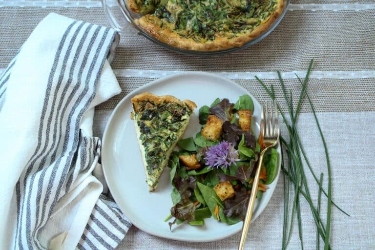 Slice of quiche on a plate with a salad to the side on plate.