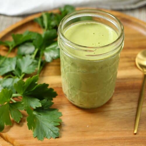 Glass jar of creamy green hummus dressing with fresh parsley to the left of the jar.