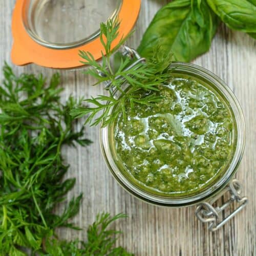 Carrot top pesto in a glass jar with flip top lid. Carrot greens and basil on surface.
