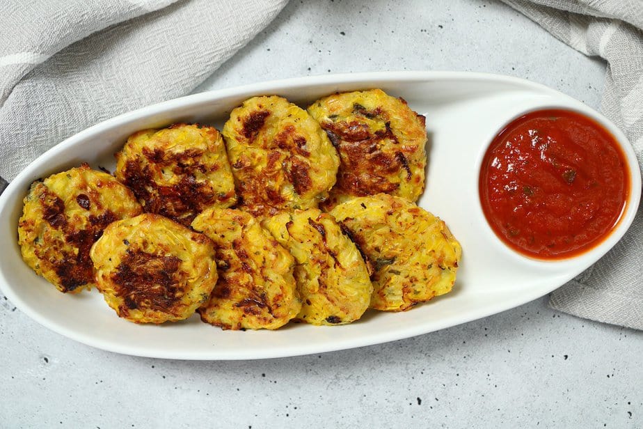 Summer squash bites in a white dish with red marinara sauce.