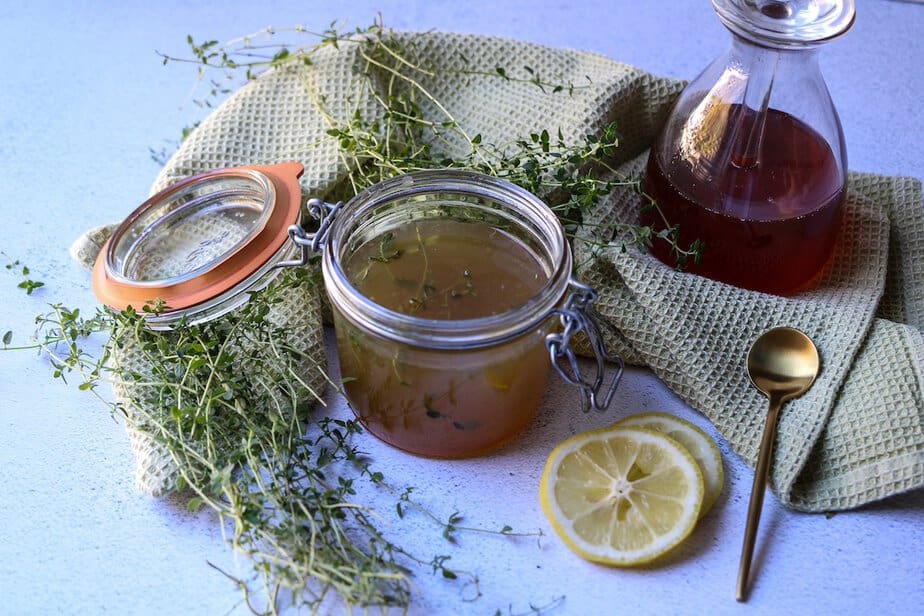 Homemade cough syrup in a glass jar with sliced lemons, fresh thyme sprigs and honey on the surface around the jar.