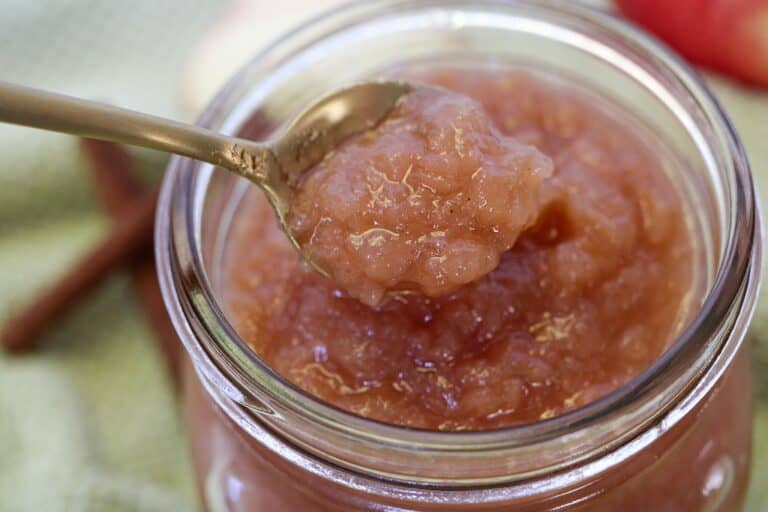 Clear glass jar of applesauce with gold spoon lifting a spoonful out.