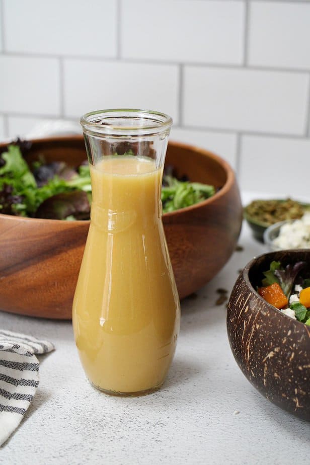 Honey Dijon Salad dressing in a clear glass jar with salad in the background.