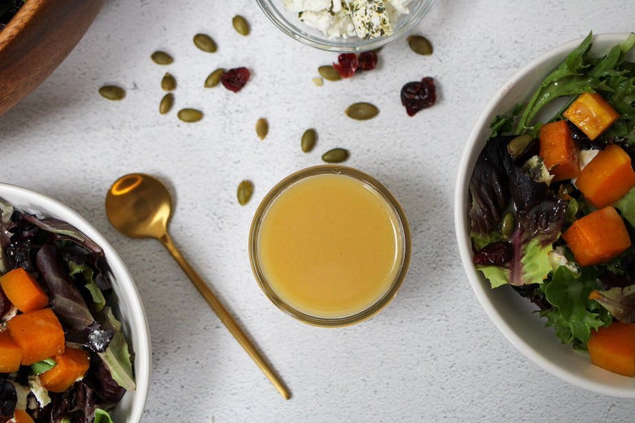 Top view honey dijon salad dressing in a jar with gold spoon and salad toppings on surface around the jar.