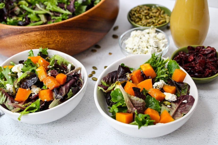 Salad greens in bowls with roasted butternut squash, crumbled goat cheese, dried cranberries and pumpkin seeds.