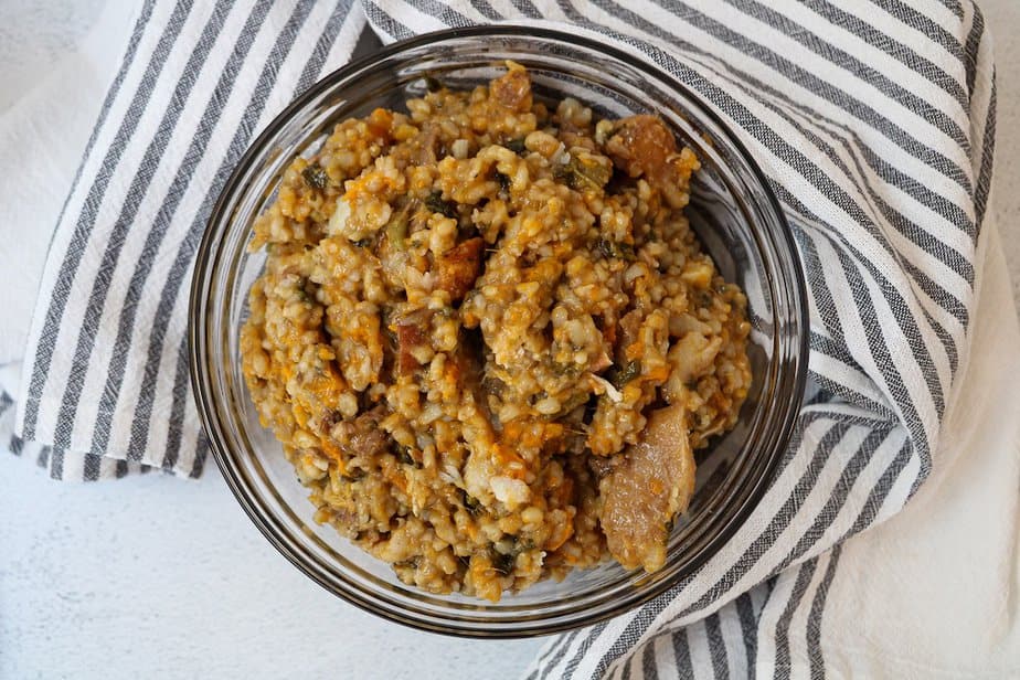 Homemade dog food in a clear glass bowl with a striped cloth around the bowl.