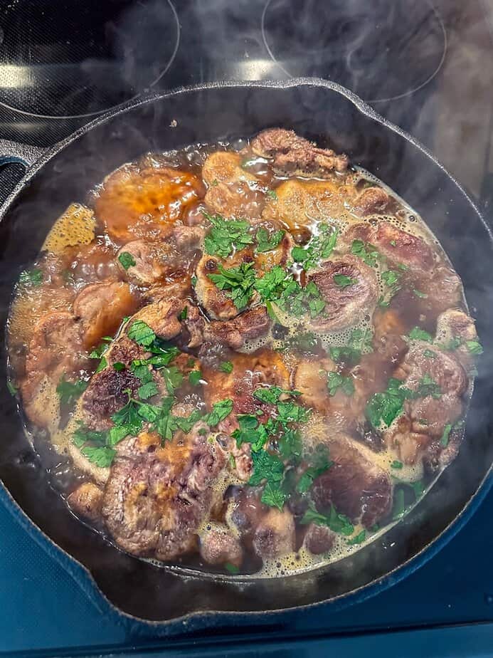 Lion's Mane mushroom steaks simmering in a broth in a cast iron pan.