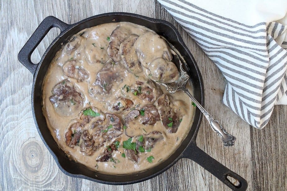 Lion's Mane Mushroom Steaks in a creamy gravy in a cast iton pan with a spoon scooping into the gravy.