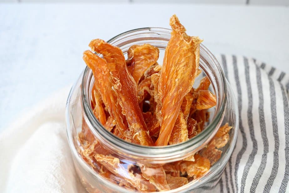 Dehydrated chicken jerky strips in a glass container.