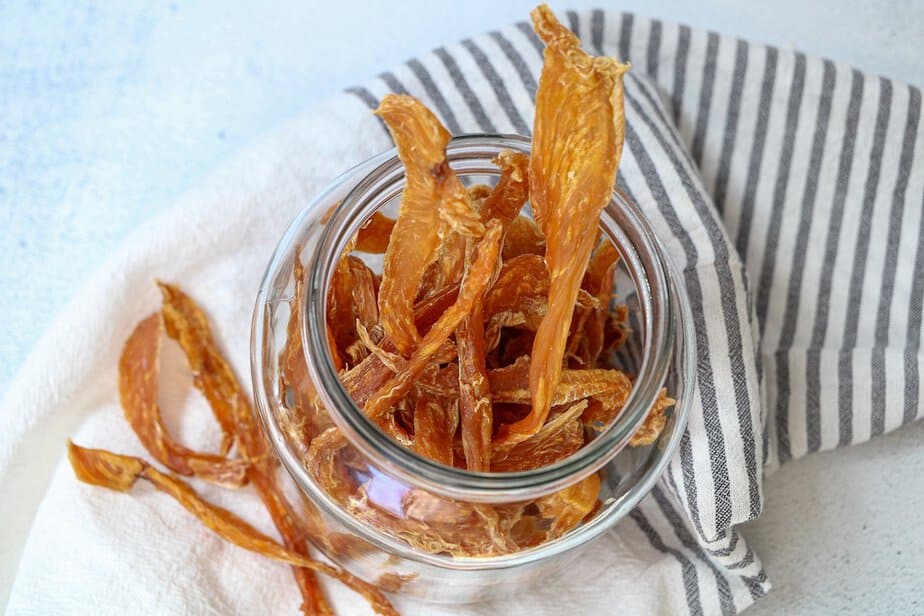 Dehydrated chicken jerky strips in a glass container.