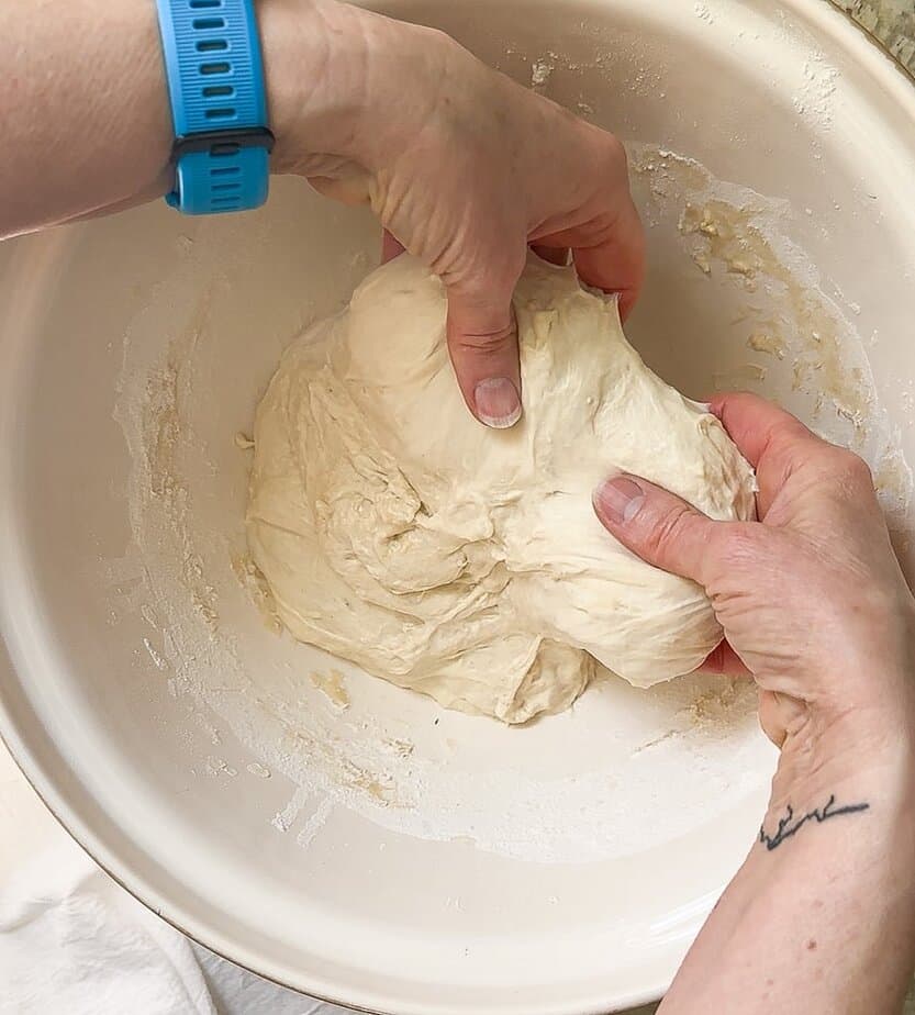 Hands lifting dough in upward motion.