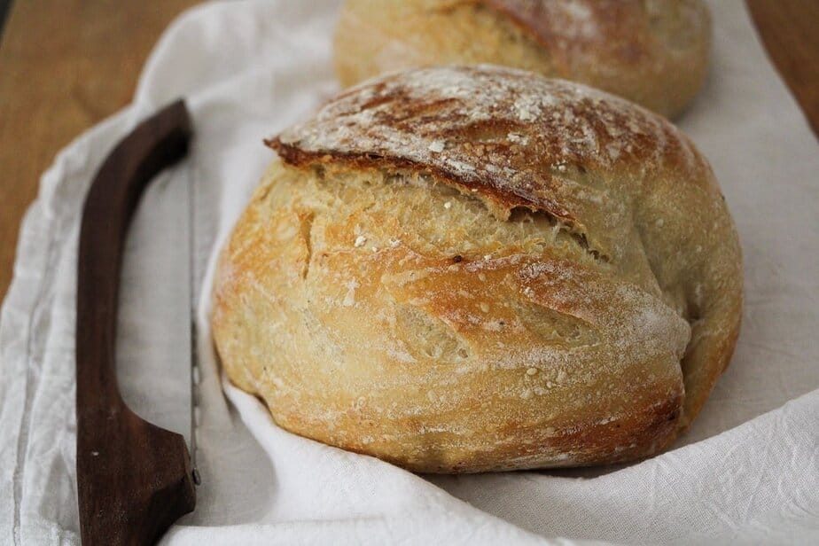 A round loaf of sourdough bread on a white bread cloth.