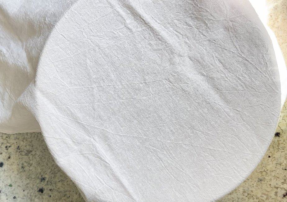 White kitchen towel covering bowl of sourdough.