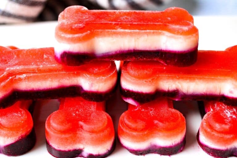Red, White and Blue layered frozen dog treats in dog-bone shapes on a white plate.