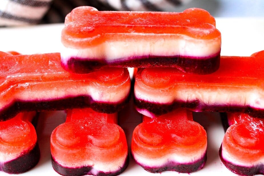 Red, White and Blue layered frozen dog treats in dog-bone shapes on a white plate.